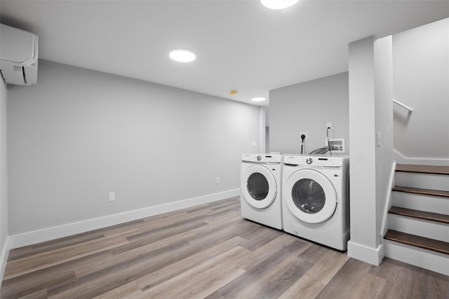 laundry area with baseboards, laundry area, an AC wall unit, washer and dryer, and light wood-type flooring