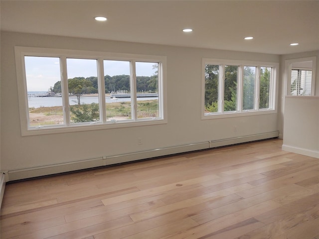 empty room with a baseboard heating unit, plenty of natural light, a water view, and light wood-type flooring