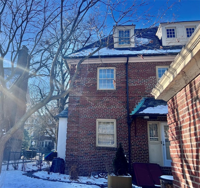 snow covered property featuring brick siding and fence