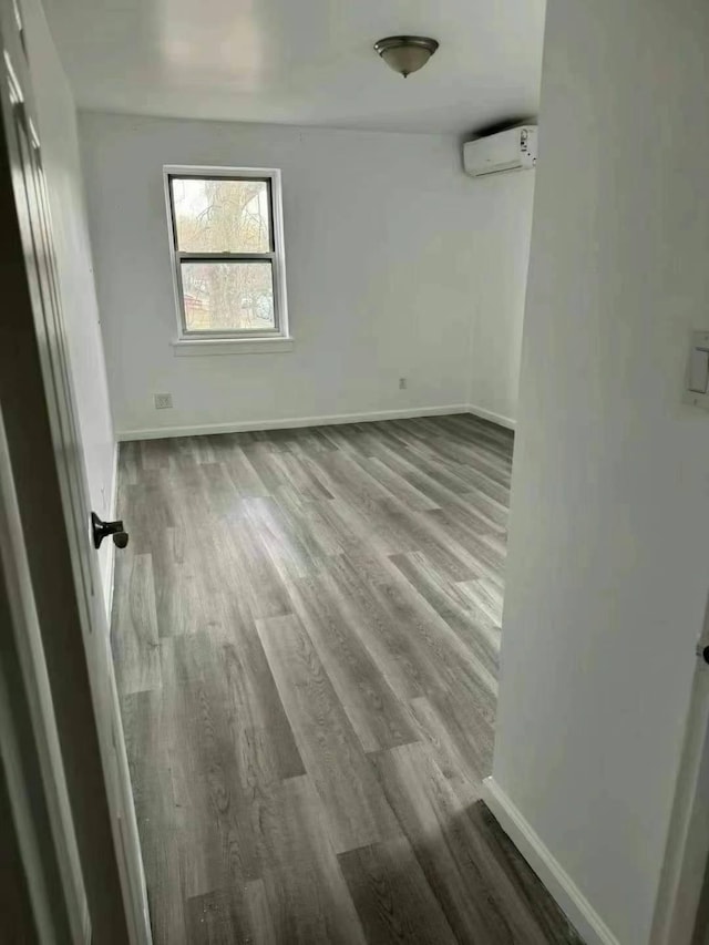 unfurnished bedroom with baseboards, wood finished floors, and a wall unit AC