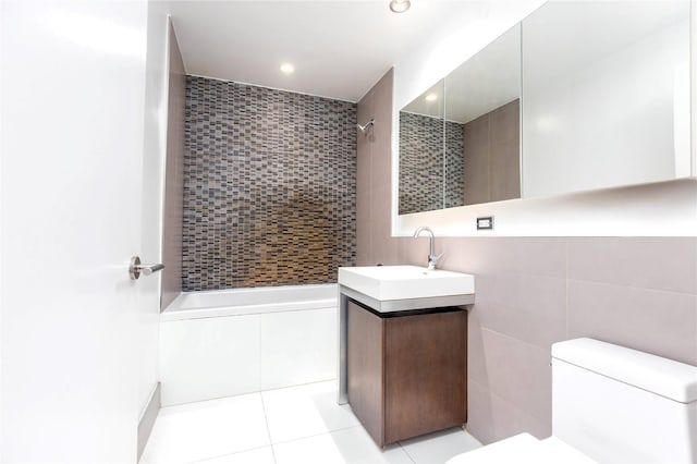 bathroom featuring tiled shower / bath, toilet, tile walls, tile patterned flooring, and vanity