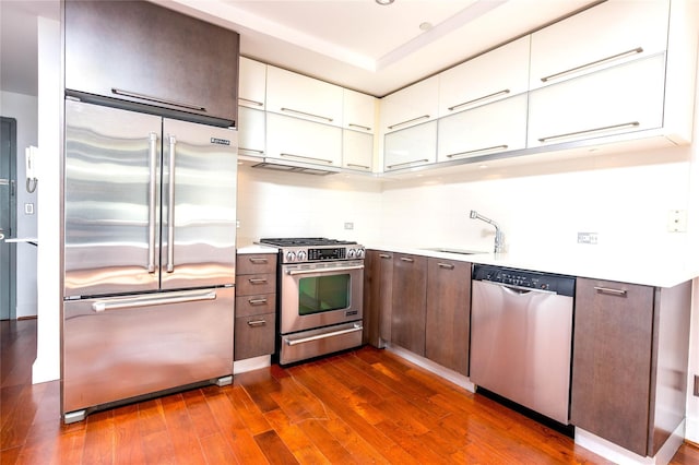 kitchen featuring dark wood-style flooring, a sink, light countertops, white cabinets, and appliances with stainless steel finishes