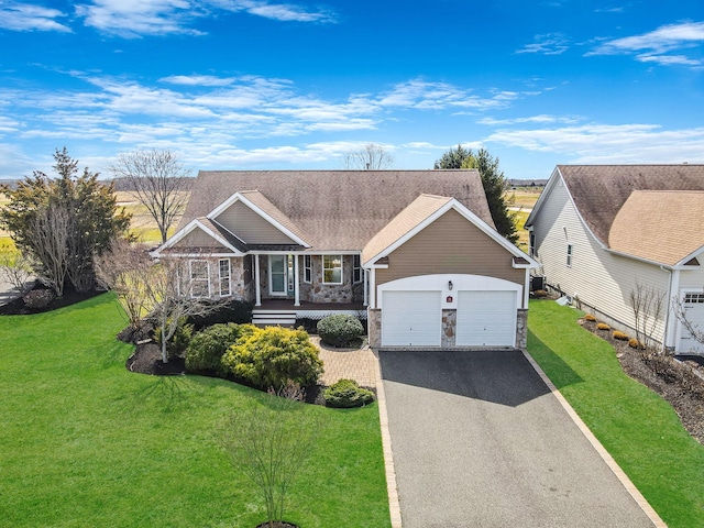 view of front of home featuring an attached garage, driveway, a front yard, and stone siding