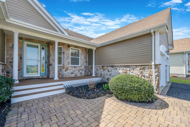 doorway to property with a shingled roof, stone siding, and covered porch