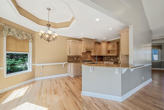 kitchen featuring a kitchen breakfast bar, tasteful backsplash, light wood-type flooring, stone countertops, and a raised ceiling