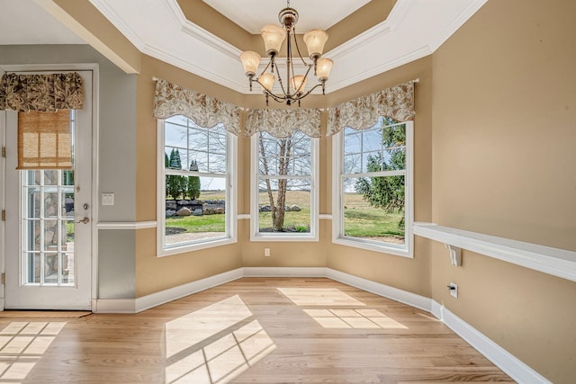unfurnished dining area featuring crown molding, a raised ceiling, a notable chandelier, and wood finished floors