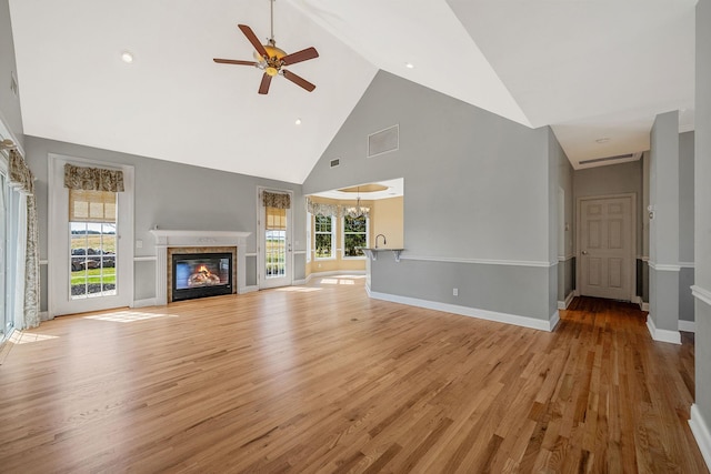 unfurnished living room with visible vents, light wood-style flooring, a glass covered fireplace, and ceiling fan with notable chandelier