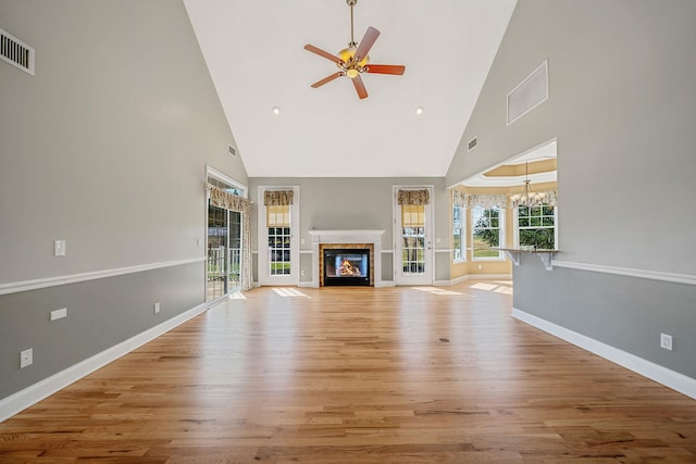 unfurnished living room featuring a glass covered fireplace, light wood finished floors, visible vents, and ceiling fan with notable chandelier