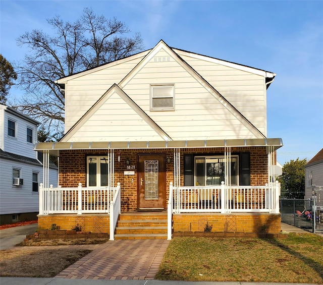 view of front facade featuring brick siding, covered porch, and fence