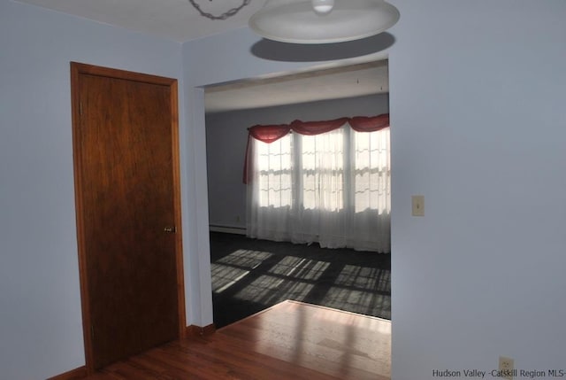 unfurnished room featuring a baseboard radiator, baseboards, and wood finished floors