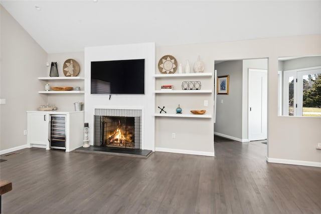 unfurnished living room featuring beverage cooler, baseboards, a lit fireplace, and dark wood-style flooring