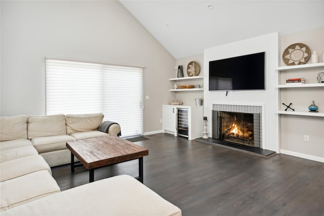 living room with built in shelves, dark wood-type flooring, beverage cooler, a warm lit fireplace, and baseboards