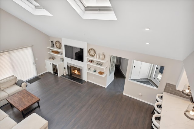 living area with a glass covered fireplace, baseboards, lofted ceiling with skylight, and dark wood finished floors