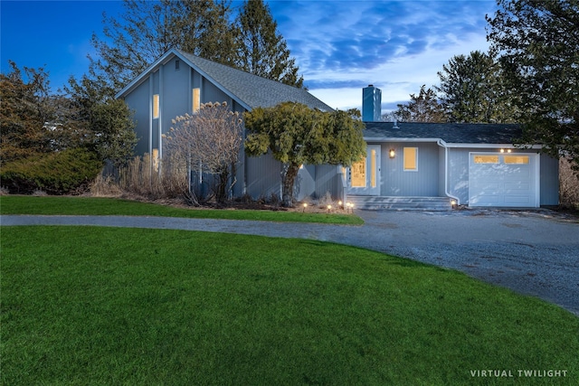 view of front of home featuring a front yard, roof with shingles, a chimney, curved driveway, and a garage