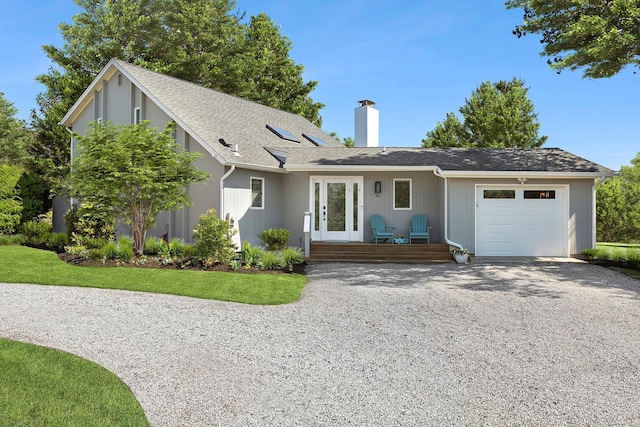 ranch-style home with a chimney, gravel driveway, an attached garage, and french doors