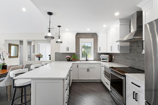 kitchen featuring a kitchen breakfast bar, stainless steel appliances, a sink, wall chimney range hood, and a peninsula