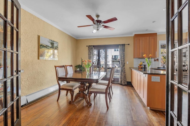 dining area featuring a baseboard heating unit, wood finished floors, ornamental molding, a textured wall, and a ceiling fan