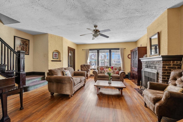 living area featuring a ceiling fan, hardwood / wood-style flooring, stairway, a fireplace, and a textured wall