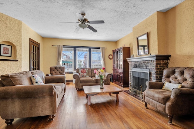 living room featuring ceiling fan, hardwood / wood-style floors, a fireplace, a textured wall, and a textured ceiling