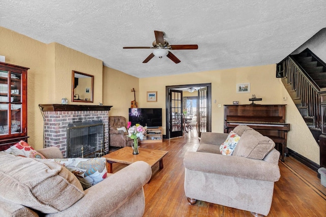 living area featuring hardwood / wood-style floors, a ceiling fan, a fireplace, stairs, and a textured ceiling