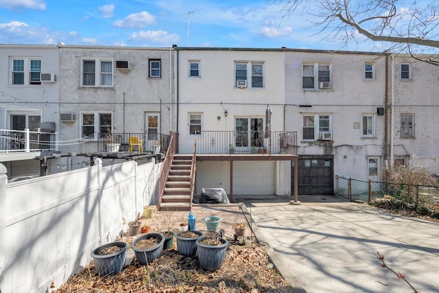 back of property featuring stucco siding, fence, concrete driveway, a garage, and stairs