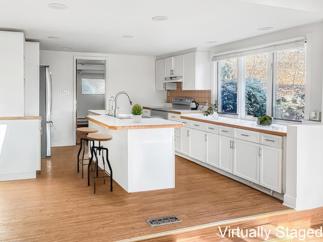 kitchen featuring electric range, a center island with sink, a sink, under cabinet range hood, and freestanding refrigerator