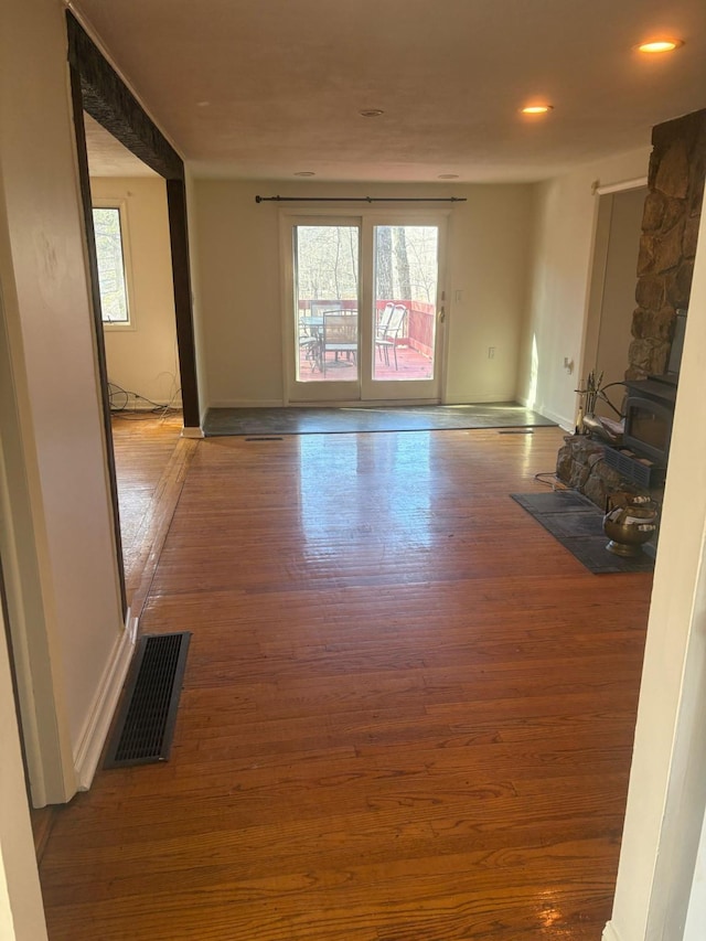 unfurnished living room with visible vents, a wood stove, baseboards, and wood finished floors