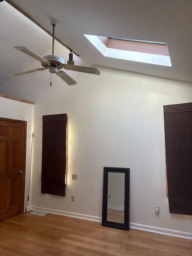 spare room with lofted ceiling with skylight, visible vents, light wood-type flooring, and ceiling fan