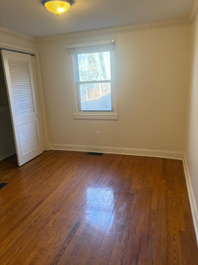 unfurnished bedroom featuring dark wood-style floors, baseboards, a closet, and ornamental molding