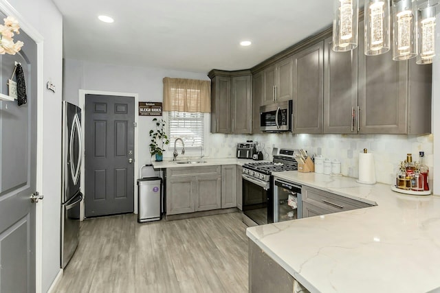 kitchen with light stone counters, light wood finished floors, a sink, stainless steel appliances, and tasteful backsplash