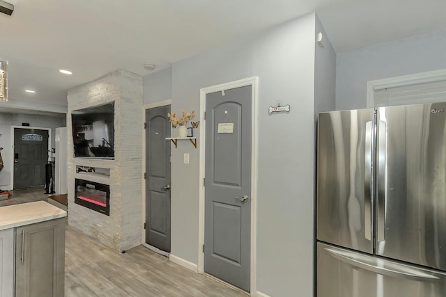 kitchen featuring light wood finished floors, a large fireplace, baseboards, light countertops, and freestanding refrigerator