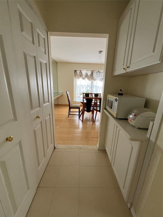 corridor with light tile patterned flooring and a notable chandelier