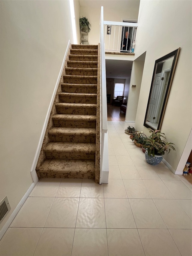 stairway with baseboards, visible vents, a high ceiling, and tile patterned flooring