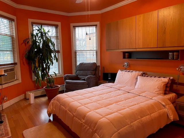 bedroom with baseboards, wood finished floors, ornamental molding, and a baseboard heating unit