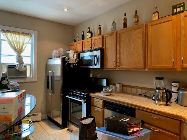 kitchen with tile counters, baseboard heating, cooling unit, light tile patterned flooring, and stainless steel appliances