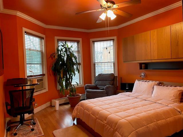 bedroom with a baseboard radiator, baseboards, light wood-style flooring, and crown molding