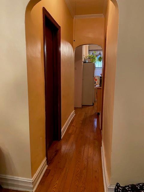 hallway featuring hardwood / wood-style floors, crown molding, baseboards, and arched walkways