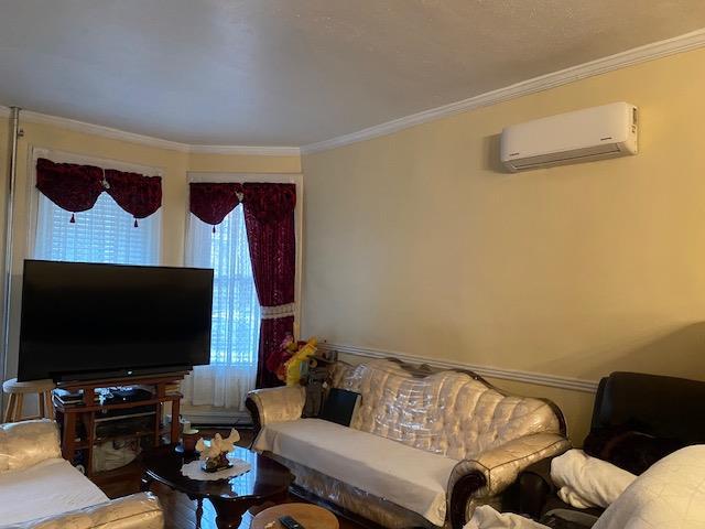 living room featuring a wall mounted air conditioner and ornamental molding