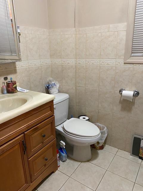 half bathroom with tile patterned floors, toilet, tile walls, and vanity