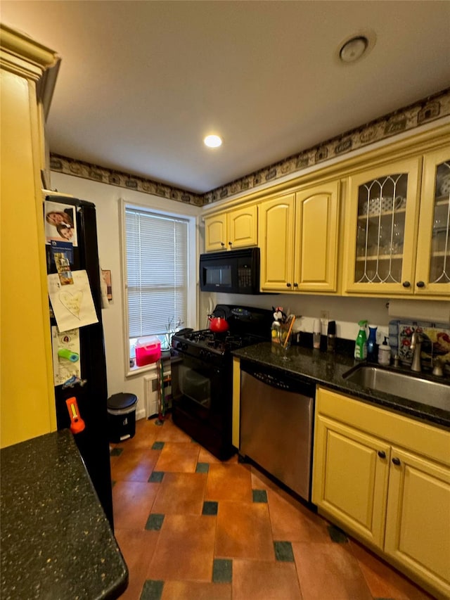 kitchen with glass insert cabinets, recessed lighting, dark stone countertops, black appliances, and a sink