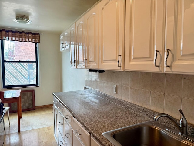 kitchen featuring dark countertops, baseboards, light wood-type flooring, decorative backsplash, and a sink