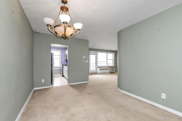 empty room with a chandelier, light colored carpet, baseboards, and radiator