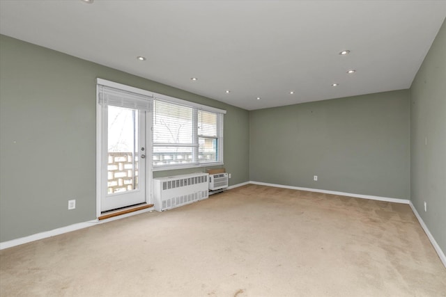 spare room featuring an AC wall unit, baseboards, recessed lighting, radiator heating unit, and light colored carpet