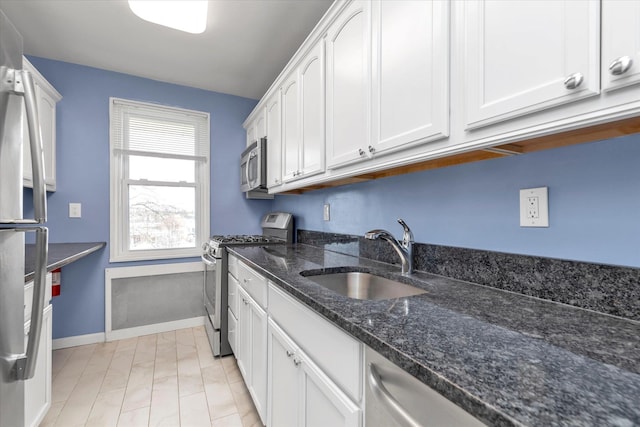 kitchen featuring white cabinetry, dark stone countertops, appliances with stainless steel finishes, a sink, and baseboards