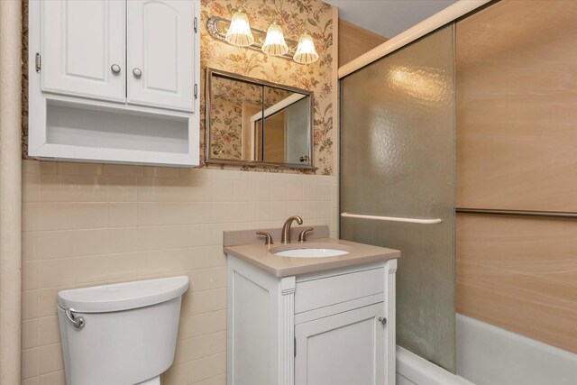 bathroom featuring toilet, tile walls, vanity, wallpapered walls, and a wainscoted wall