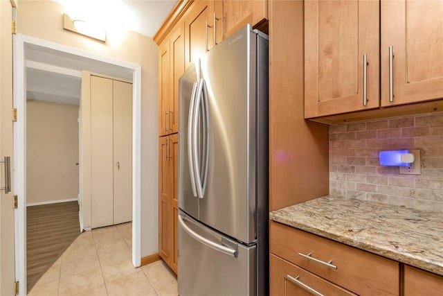 kitchen with baseboards, freestanding refrigerator, backsplash, light tile patterned flooring, and light stone countertops