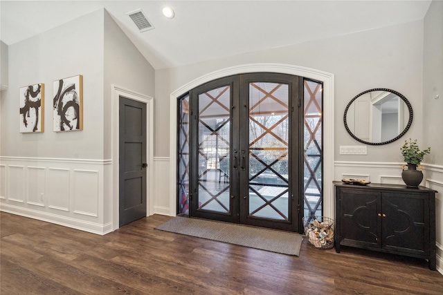 foyer entrance with wood finished floors, a wainscoted wall, visible vents, lofted ceiling, and french doors