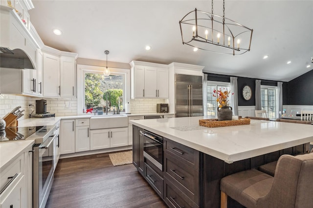 kitchen with a breakfast bar area, a sink, dark wood-type flooring, built in appliances, and white cabinetry