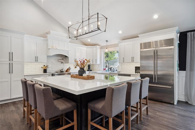 kitchen with a sink, a kitchen island, white cabinetry, stainless steel appliances, and vaulted ceiling