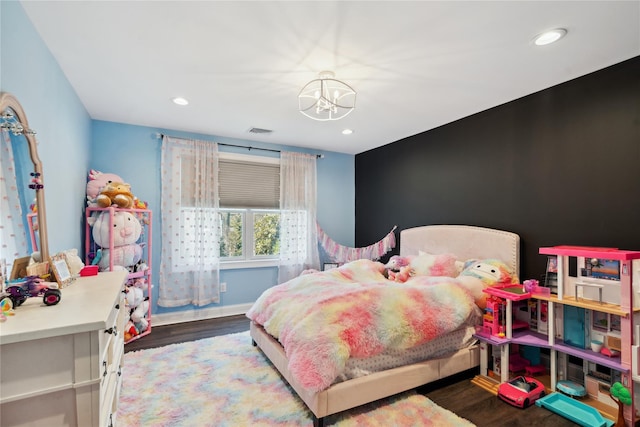 bedroom with an accent wall, wood finished floors, visible vents, and a chandelier